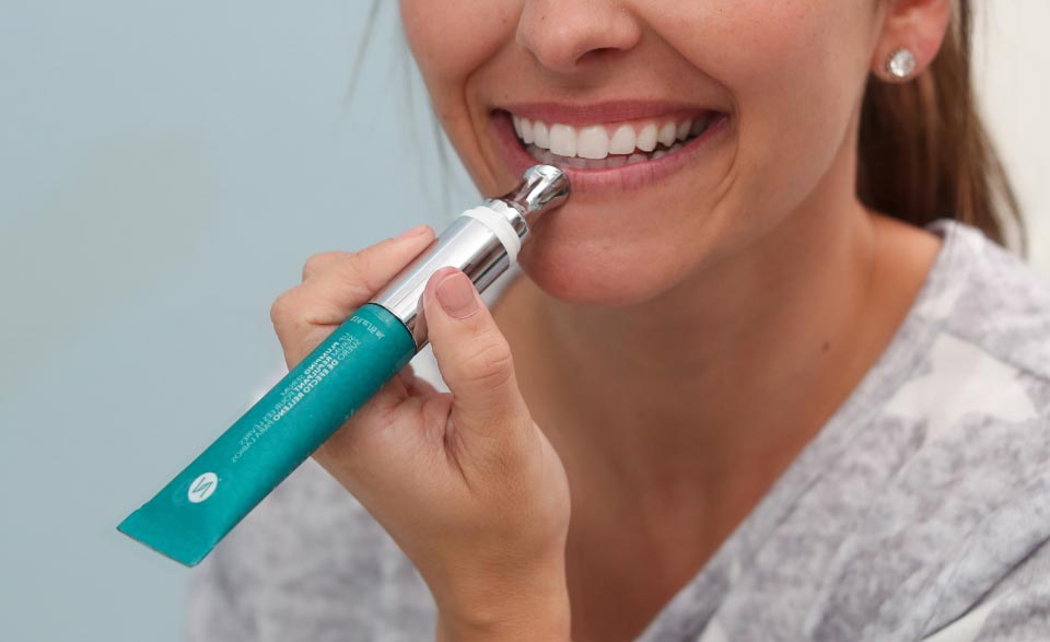 A smiling woman applying the Lip Plumping Serum on her lips.