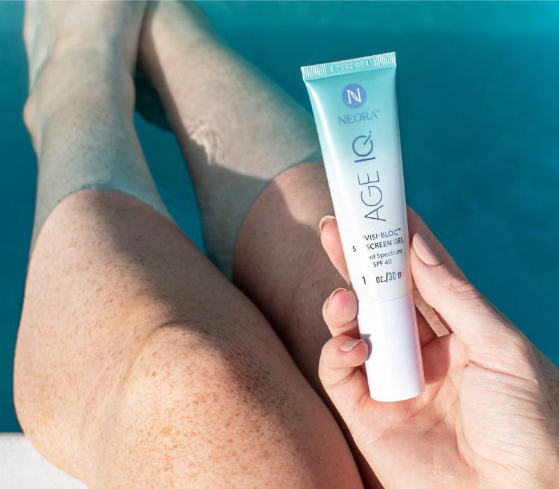 Woman holding Neora’s Age IQ® Invisi-Bloc Sunscreen Fel SPF 40 in her hands while sitting in a pool